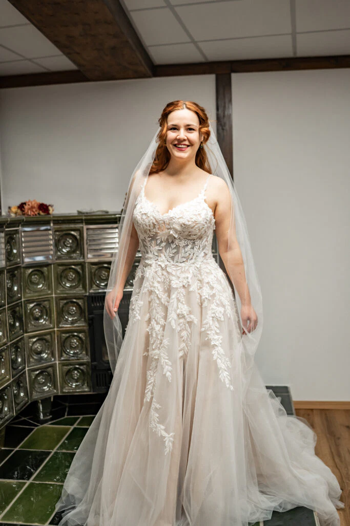 Lächelnde Braut im Hochzeitskleid vor Kamin