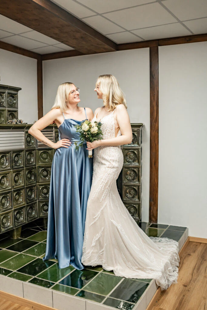 Zwei Frauen lächeln im eleganten Hochzeitskleid.