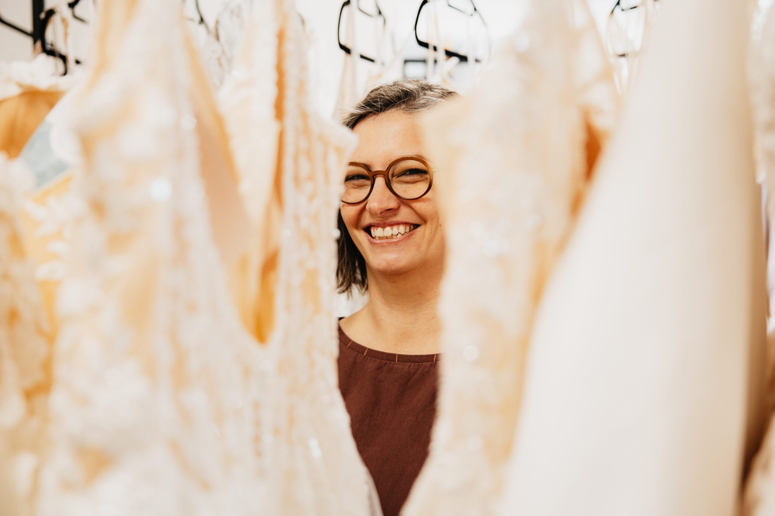 Lächelnde Person zwischen Hochzeitskleidern